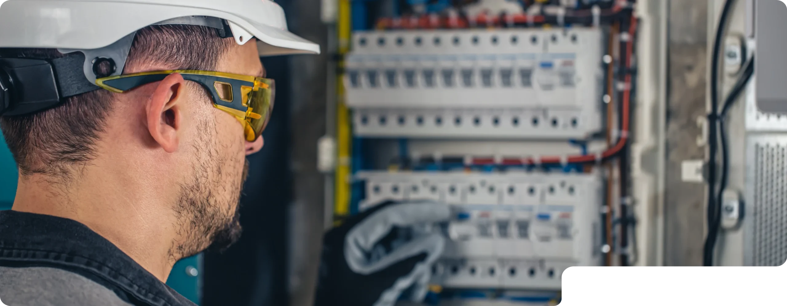 photo from behind of a man with yellow glasses who is filming him and wearing a cap while looking at an electrical panel